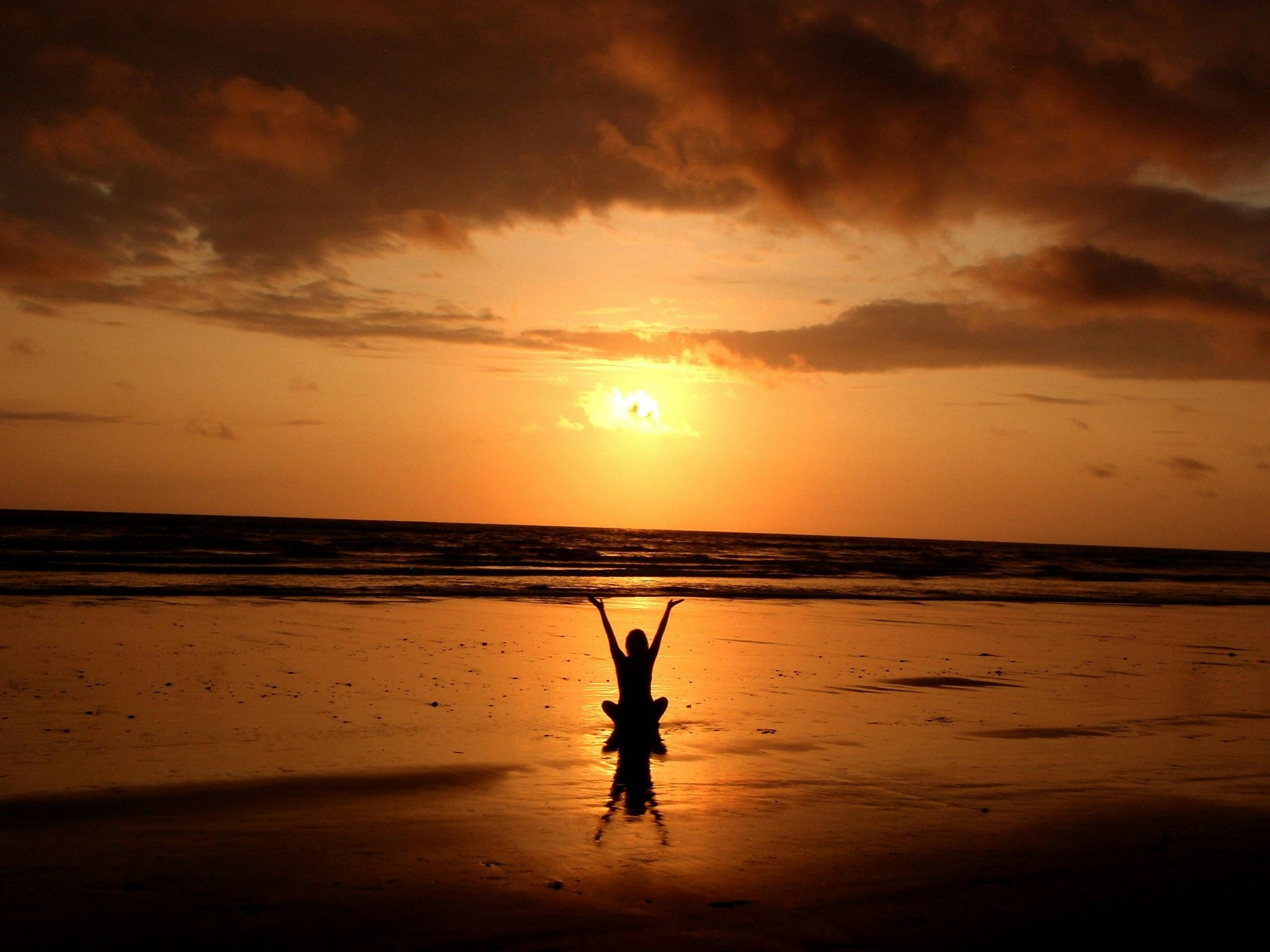 An image of a woman in silhouette, connecting with herself while the sun is setting down.