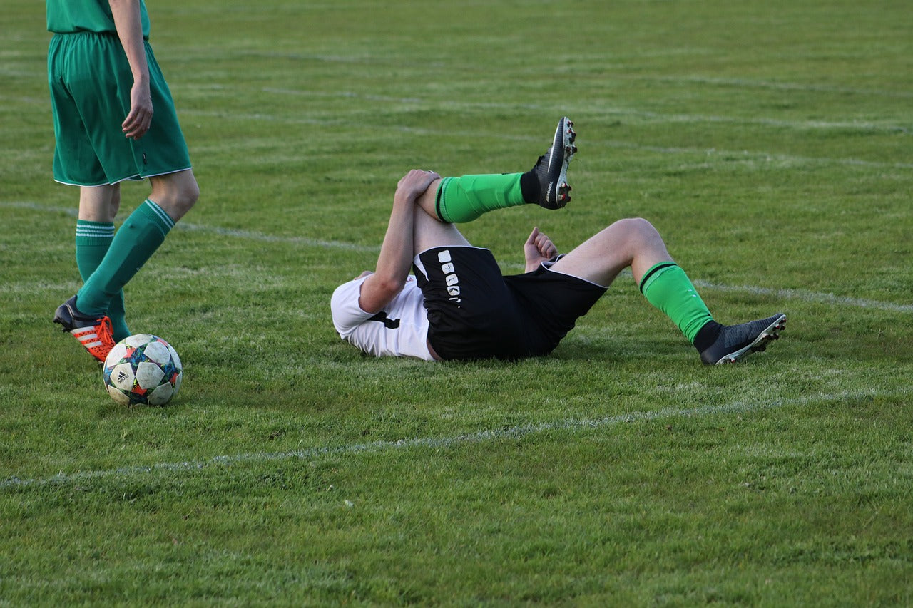 An image of a man experiencing sports injury in a footbal field, e.g. muscle sprain.