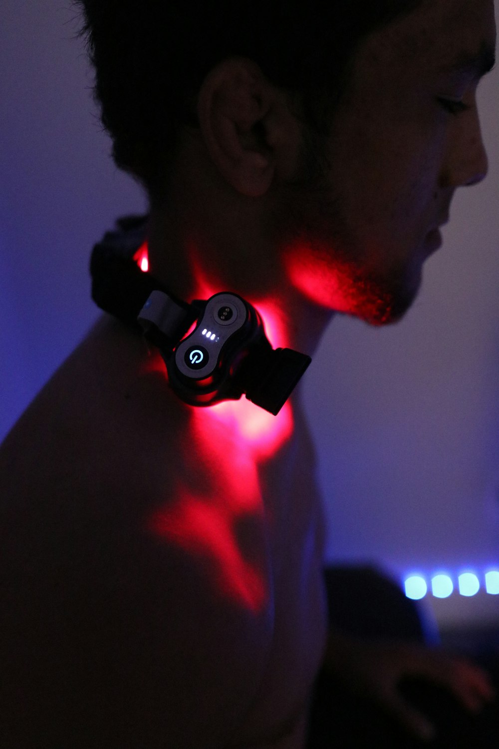 A man using a red light therapy device on his neck.