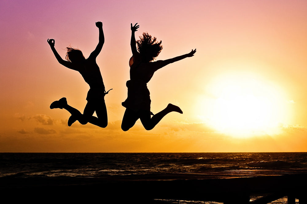 An image of 2 women jumping in happiness in the sunset.