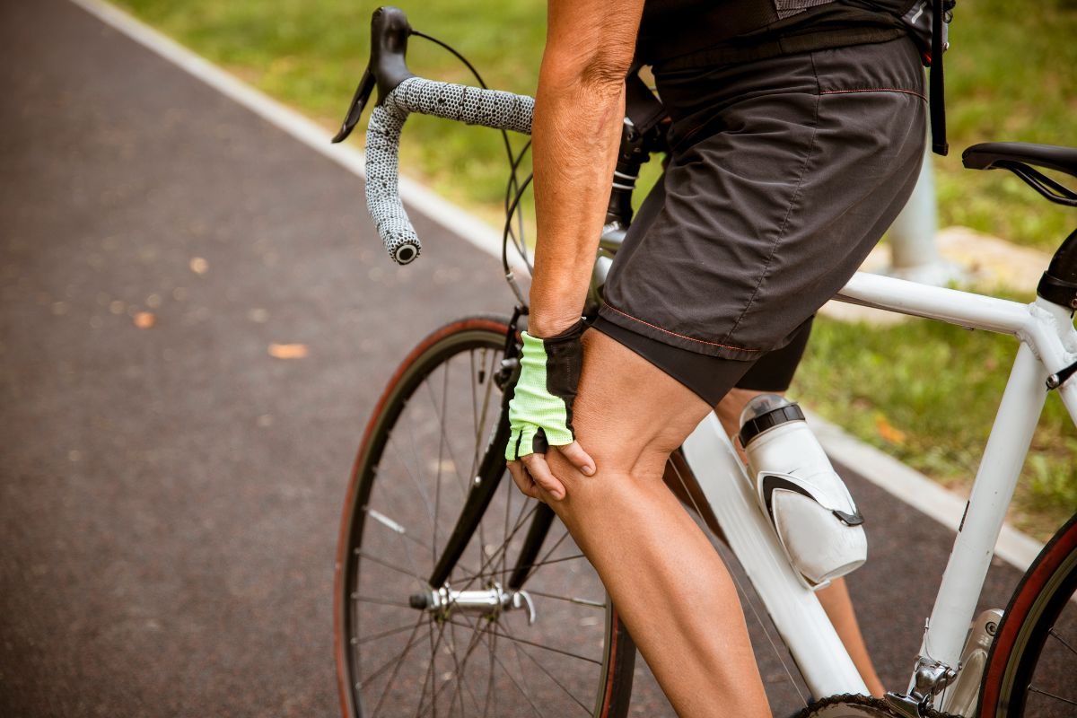 Cyclist pausing on the road, holding a sore knee